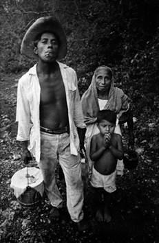Camino a su casa, después de la ceremonia del Ch’a Cháak, Darío fuma un cigarro hecho por él mismo (u chamal yum cháak) con tabaco nativo y lleva un cubo de comida ceremonial. Su madre y su hijo José lo acompañan. Chichimilá. 1971.